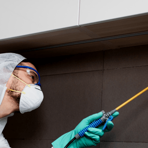 Contractor wearing PPE and mask cleaning cabinet with chemicals