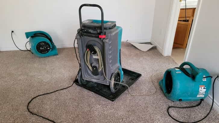 twon blue air movers and a dehumidifier drying a carpet from a water damage flood job
